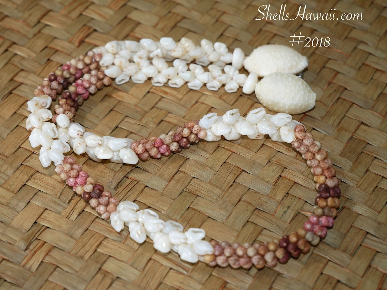 Finished handmade Hawaiian shell lei featuring Kahelelani, Momi, and off-white Granulated Cowrie shells arranged on a woven lauhala mat.
