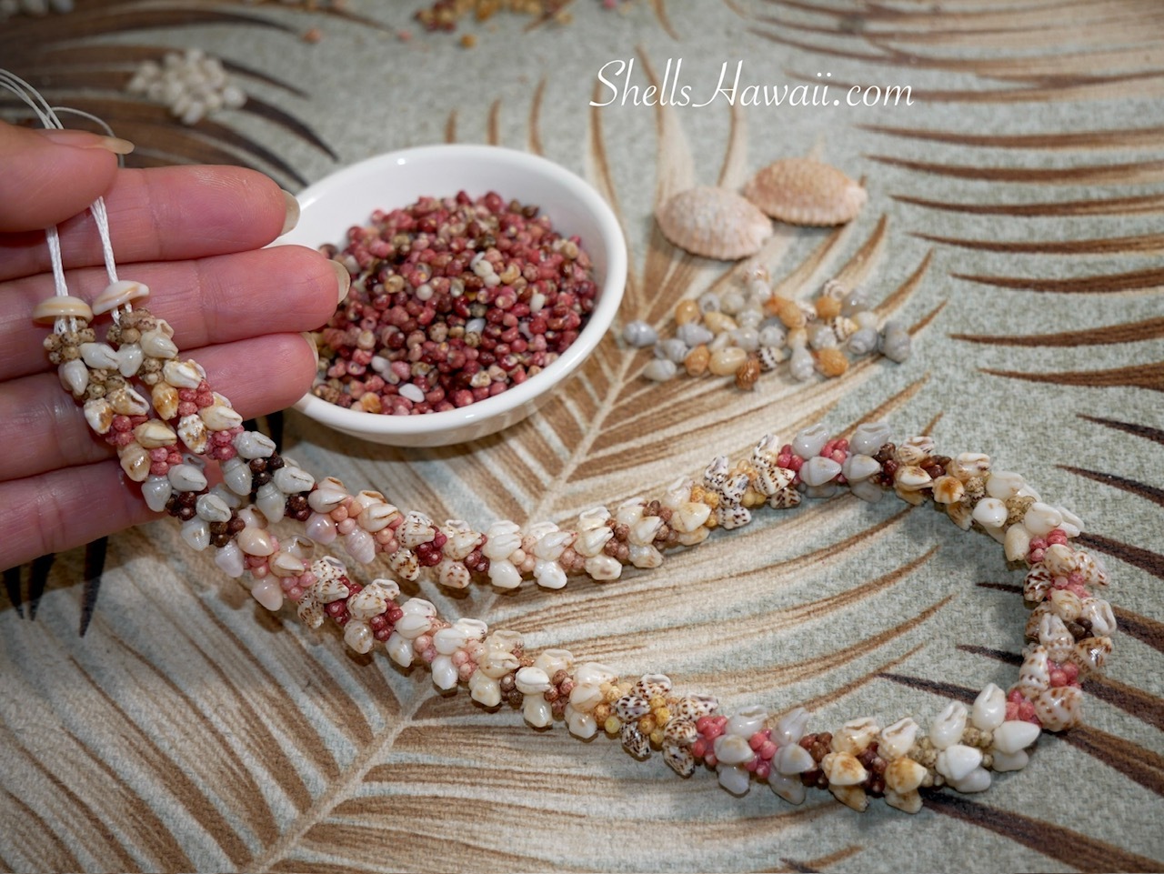 Hand-held view of a nearly finished Niʻihau Kipona style shell lei made with natural Momi and colorful Kahelelani shells before adding the clasp.