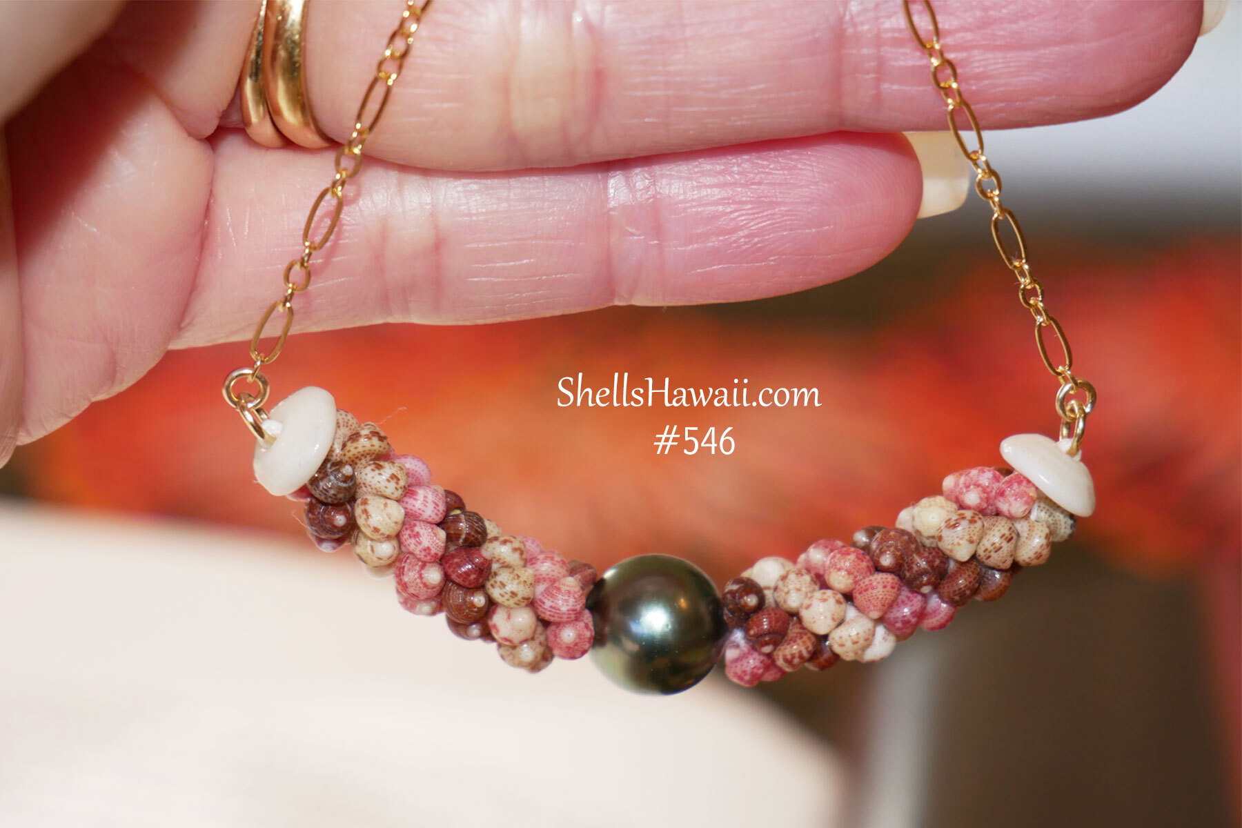 A minimalist Niʻihau shell necklace design featuring pink, green, red burgundy Kahelelani shells with a Tahitian pearl centerpiece on a gold filled chain, perfect for everyday wear.