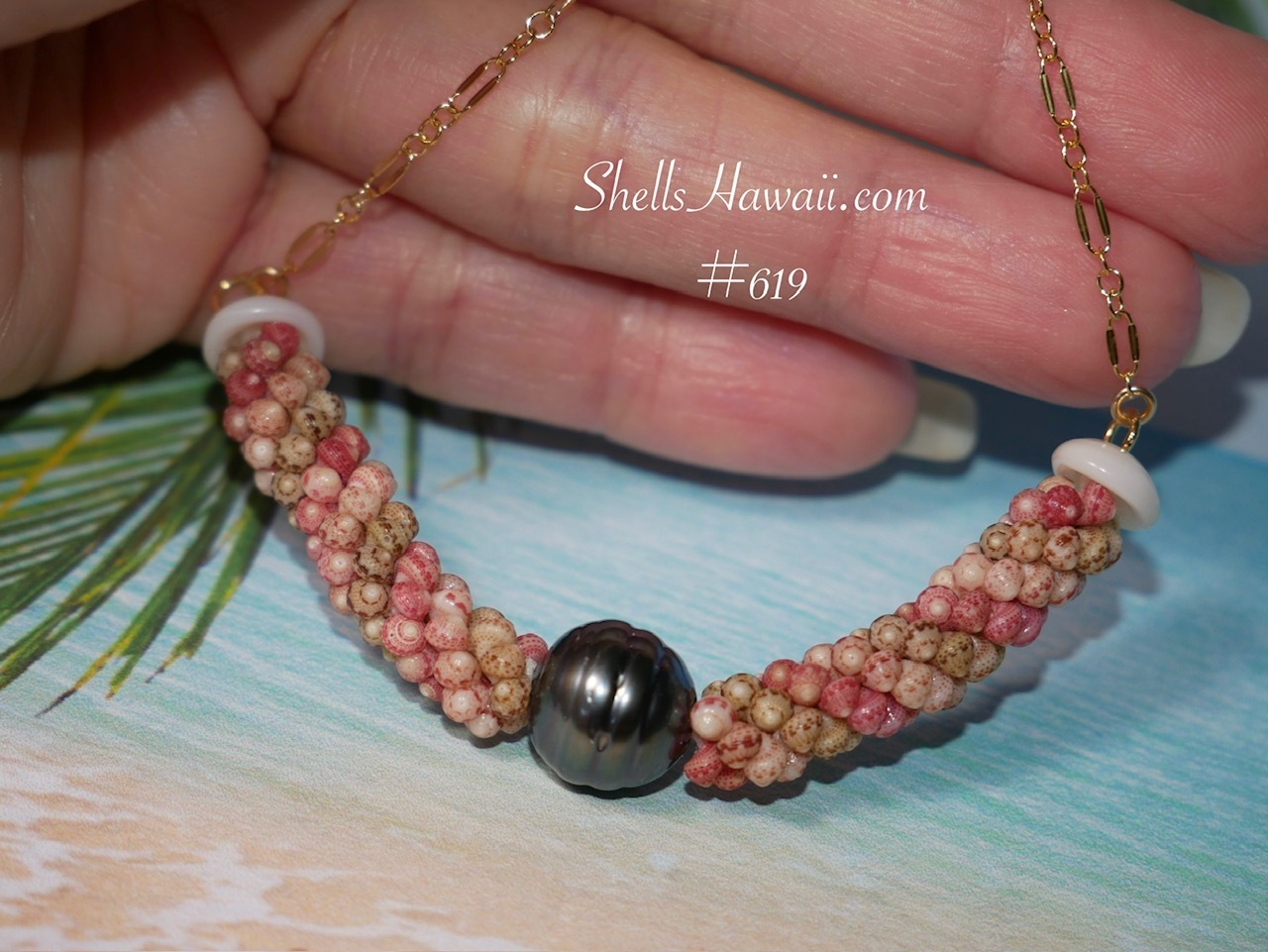 Close-up photograph of handcrafted Triple Poepoe style Niʻihau shell jewelry necklace created with genuine Kahelelani shells from Niʻihau. The necklace features a soft spiral rope-like structure with natural shell colors including ʻĀkala Pua pink flower, ʻŌmaʻomaʻo green, and Keʻokeʻo white surrounding a dark Tahitian pearl centerpiece. Finished with a delicate 14k gold filled chain and white Momi shell accents.