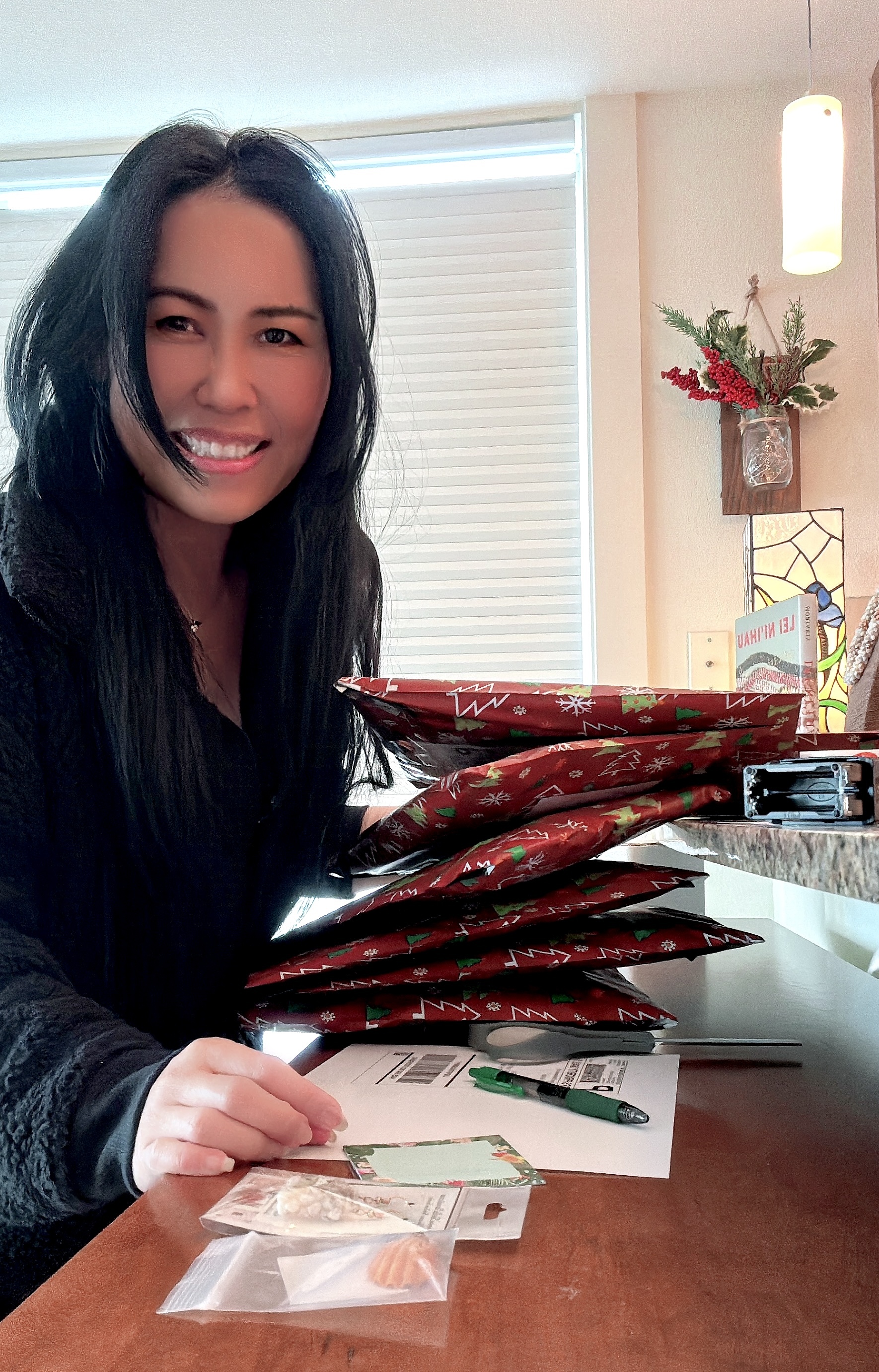 Janjira packing holiday orders with care, holding wrapped Niʻihau shell jewelry gifts at her workspace, sharing gratitude during the holiday season.