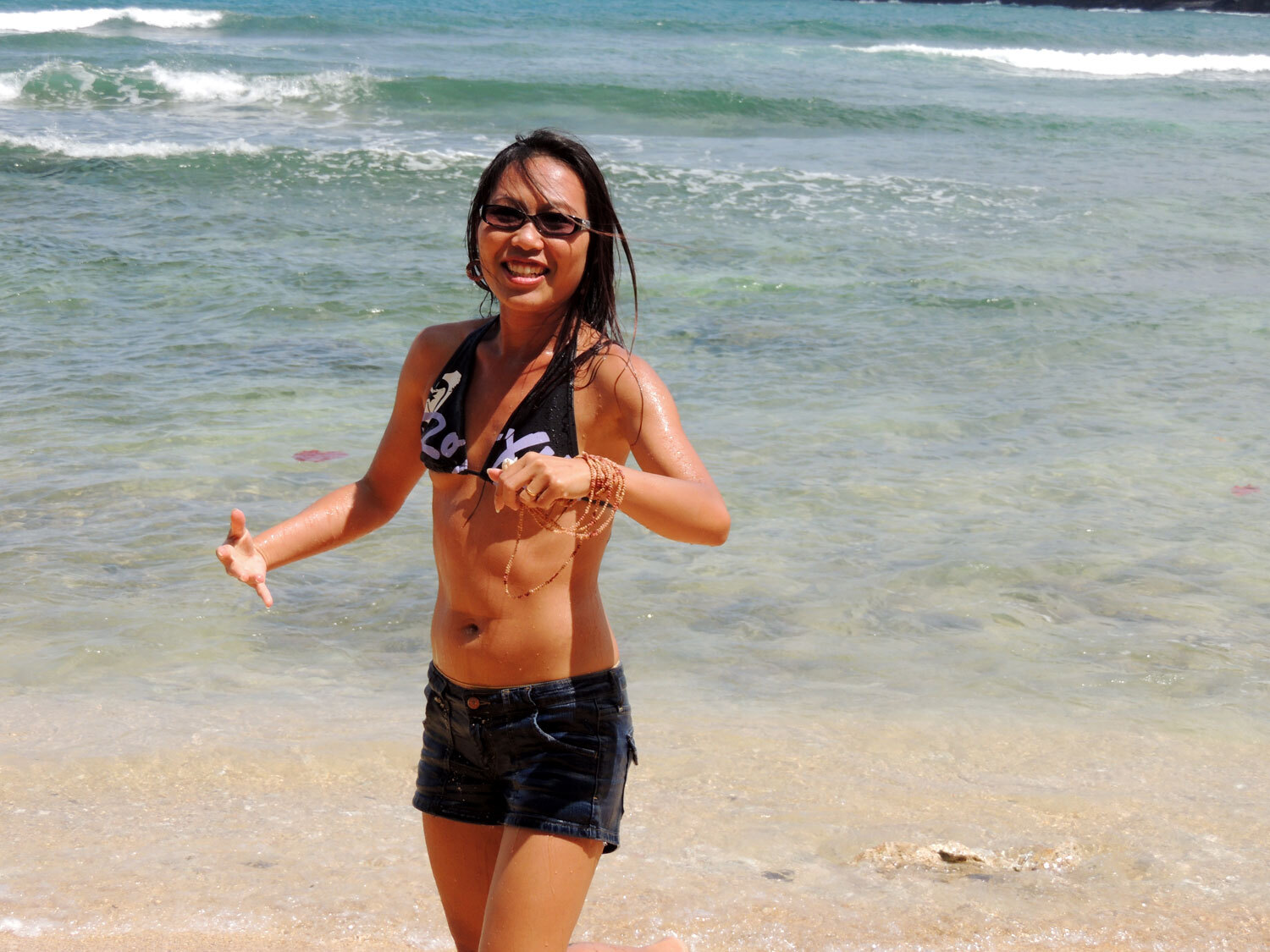Behind-the-scenes moment of Janjira from ShellsHawaii.com enjoying the waves at a Kauaʻi beach while photographing her Niʻihau shell jewelry.