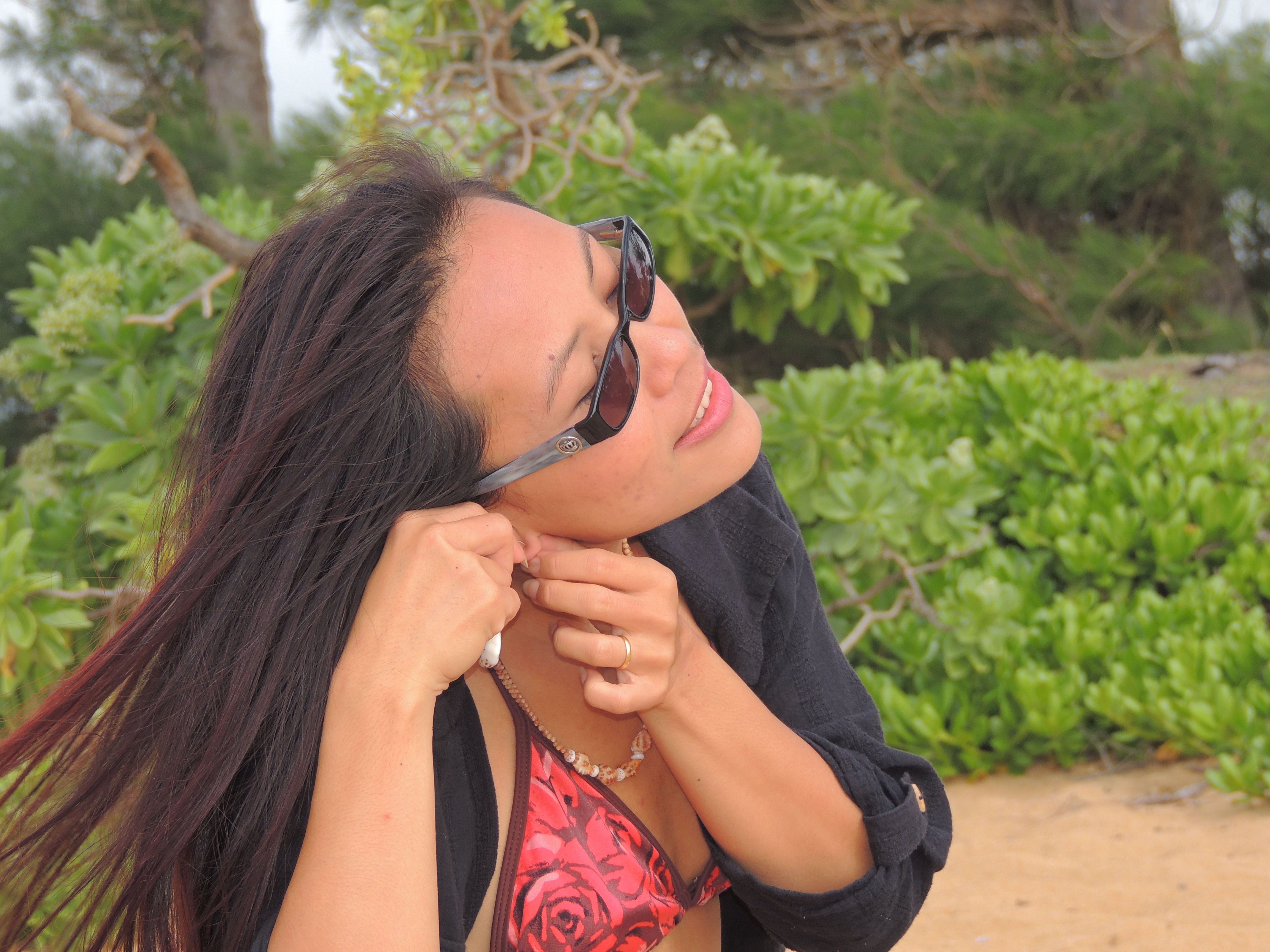 ShellsHawaii.com owner Janjira putting on Niʻihau shell earrings during a Kauaʻi beach photoshoot for her handmade Hawaiian jewelry collection.