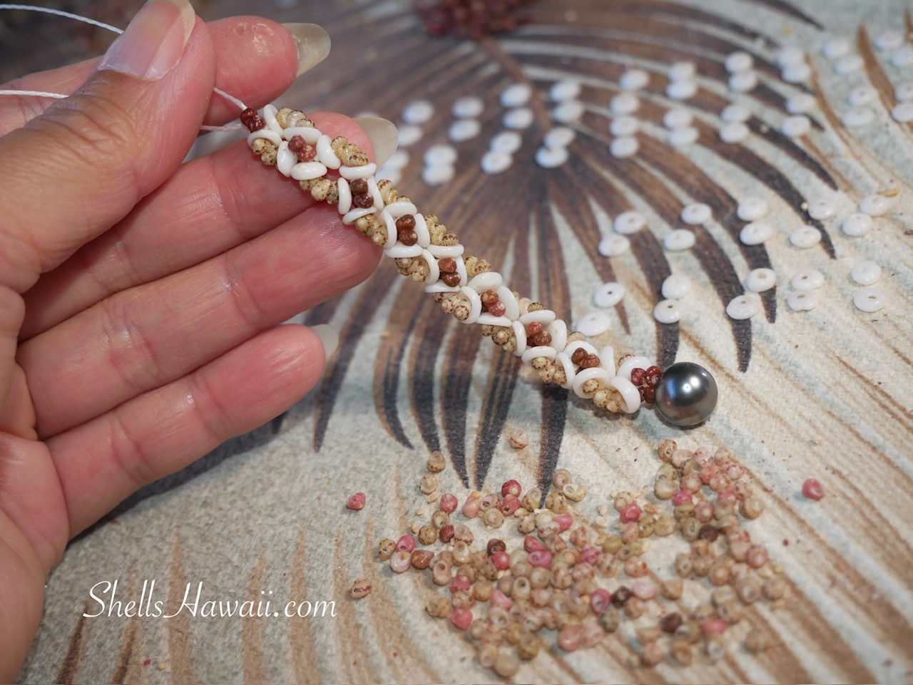 Close-up of a finished pair of flower-inspired Hawaiian shell earrings handcrafted with genuine green and brown Kahelelani shells from Niʻihau, Hawaiian Puka shells from Kauaʻi, and a beautiful Tahitian pearl.