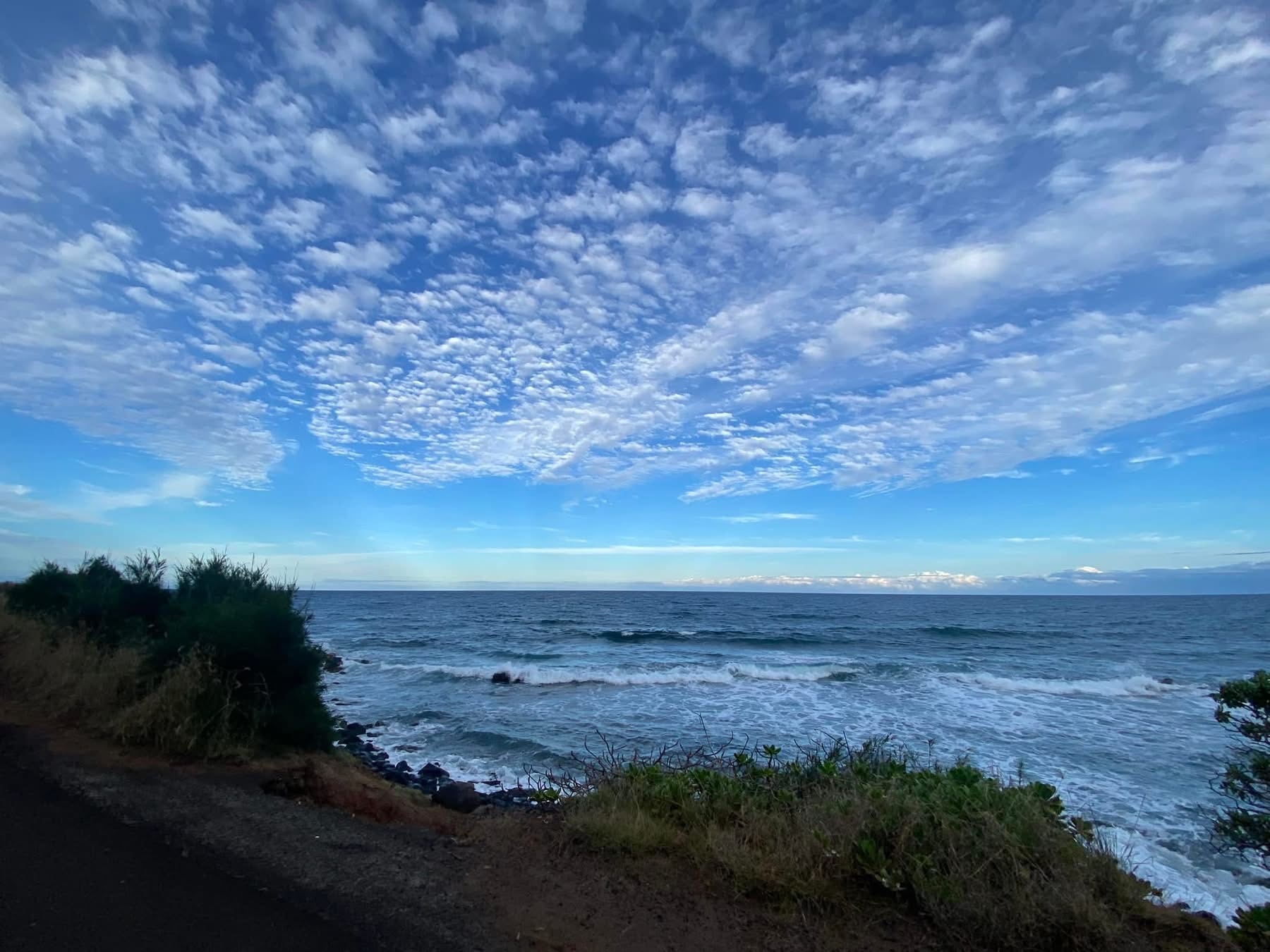 Wide Hawaiian ocean view with a bright blue sky and soft clouds above the sea, reflecting the calm, depth, and natural blue tones that inspire rare ocean-blue Momi shells and Niʻihau shell jewelry.