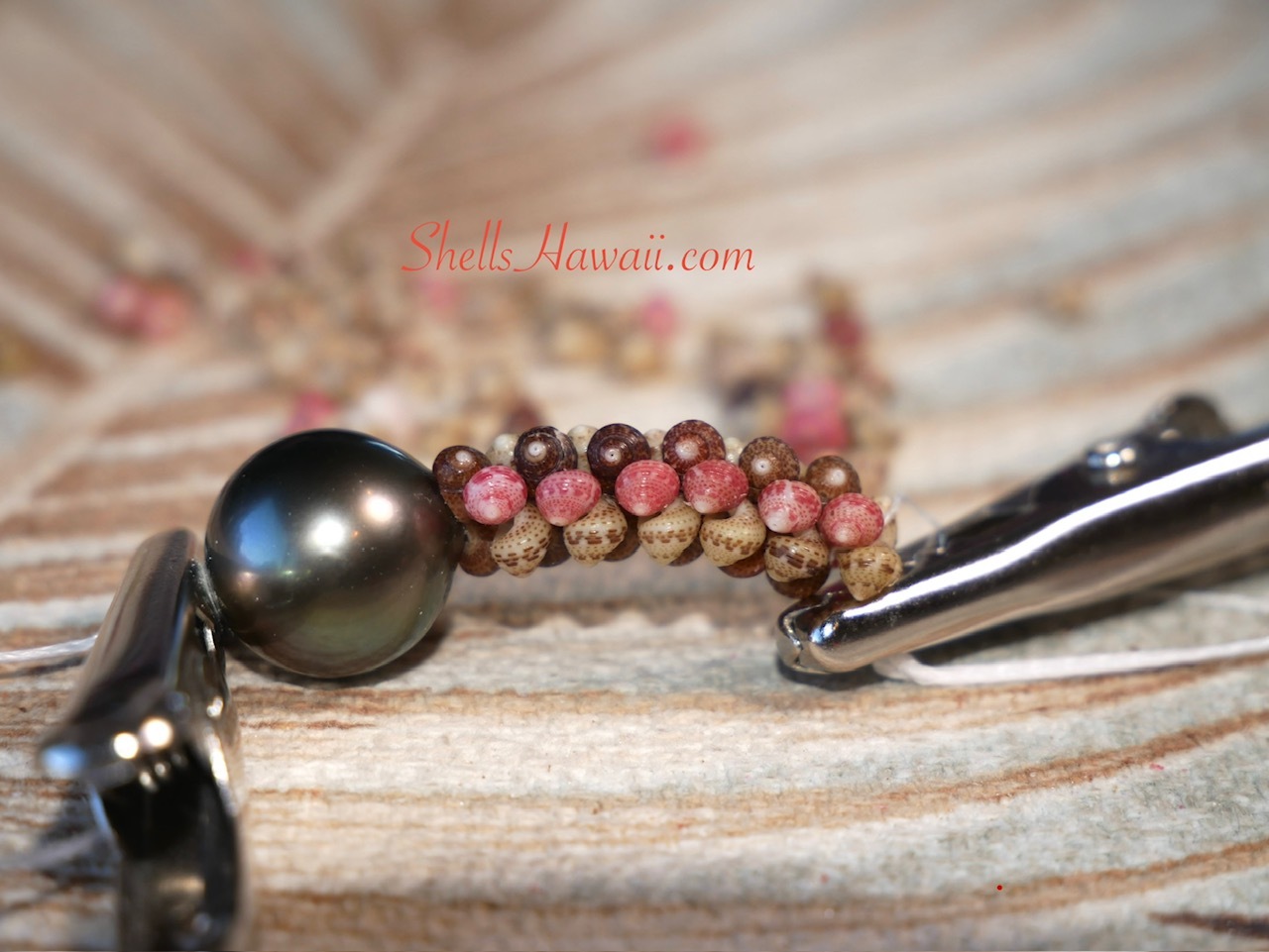 Close-up of a handcrafted Kahelelani Poepoe section showing properly aligned shells beside a Tahitian pearl on a traditional Niʻihau Kipona shell lei.