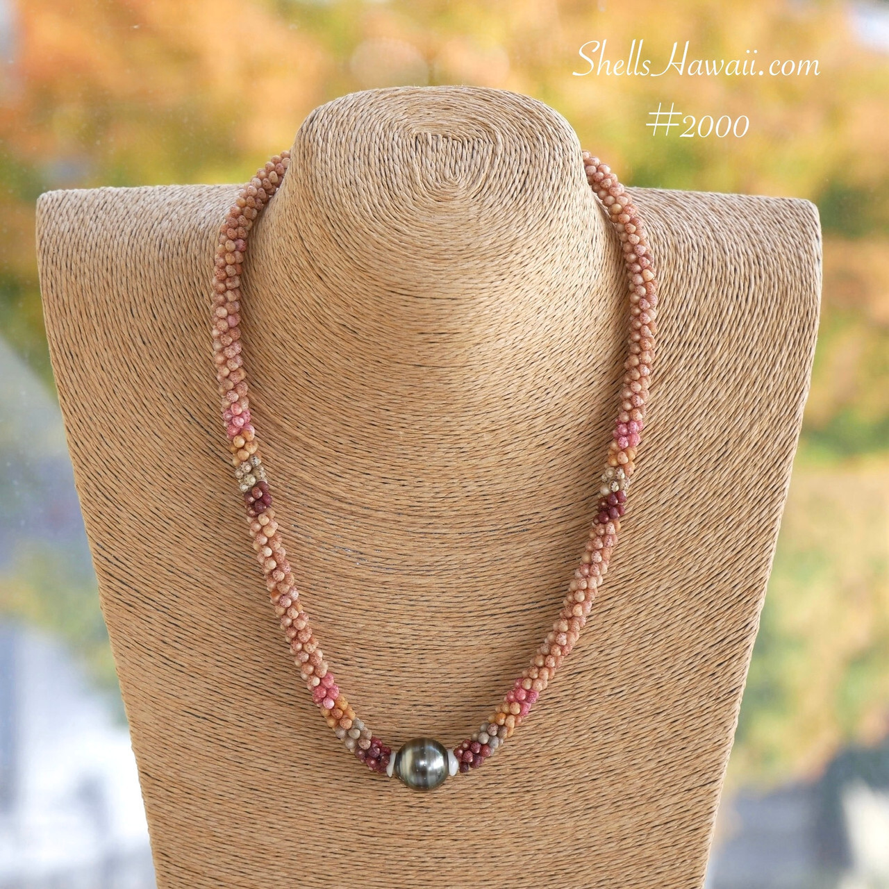 Close-up of handcrafted Hawaiian two strand Poepoe style necklace featuring tiny colorful Kahelelani shells from Niʻihau paired with a dark Tahitian pearl centerpiece in an elegant Hawaiian shell jewelry design displayed on a natural necklace bust background.