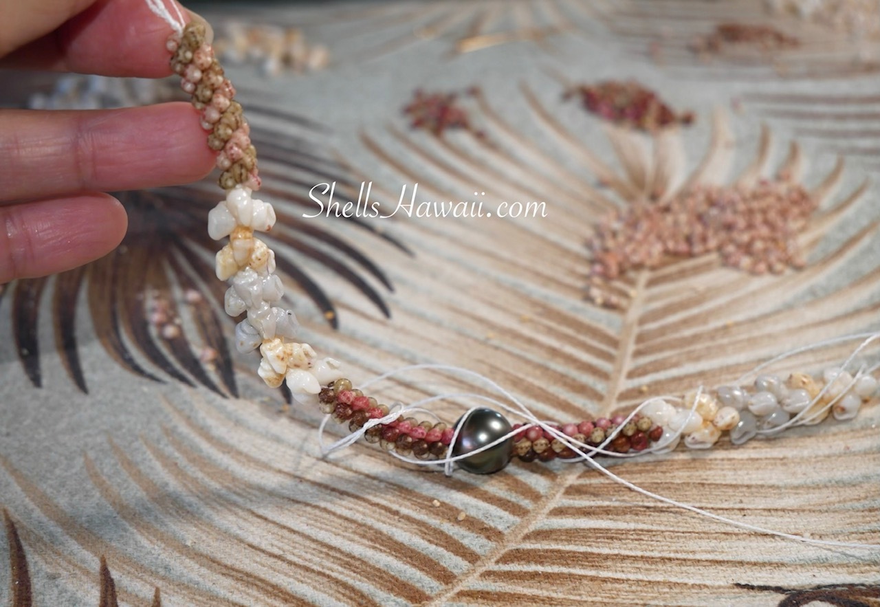 Longer traditional Niʻihau shell lei during weaving, showing the string twisting around the growing lei as tension builds during the creation process.