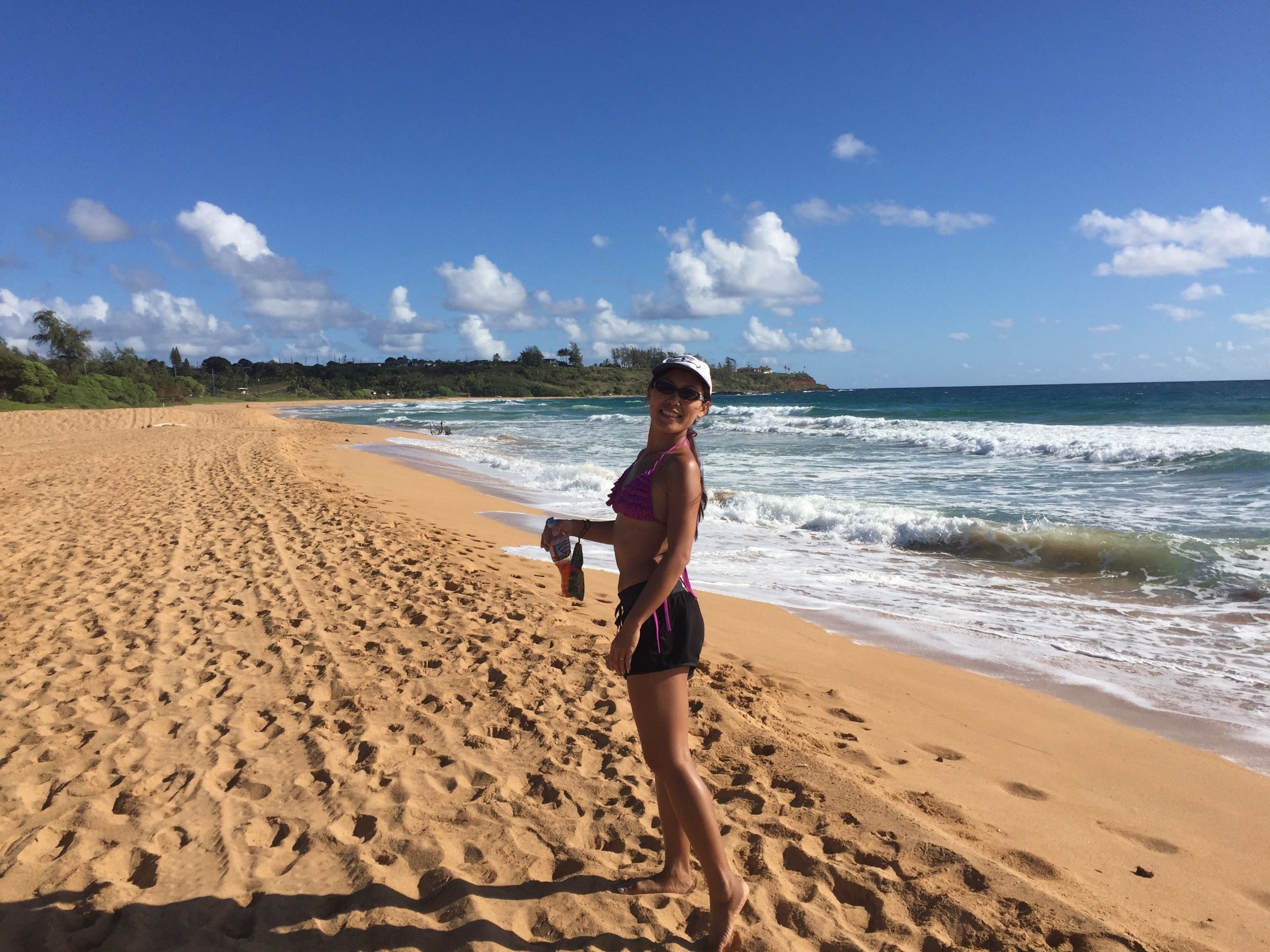 Janjira enjoying a peaceful morning walk at Keālia Beach, Kauaʻi surrounded by golden sand, blue ocean waves, and sunny Hawaiian skies