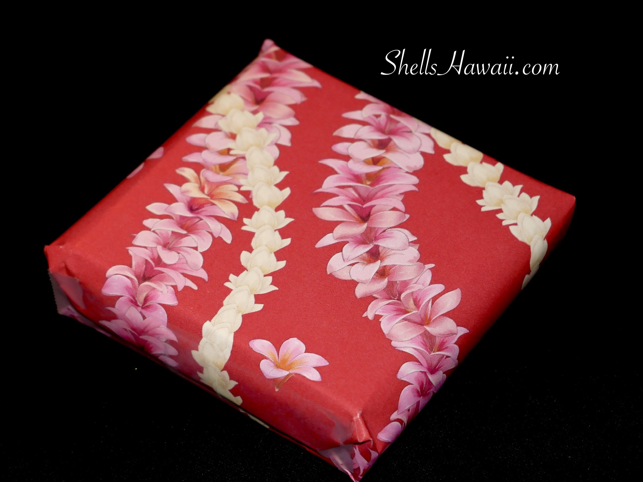 Hawaiian plumeria lei wrapping paper with layered pink and cream flower strand design on red background, festive gift wrap for Niʻihau shell jewelry